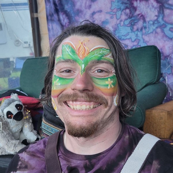 Man with face painted in the shape of flame flower and leaves.