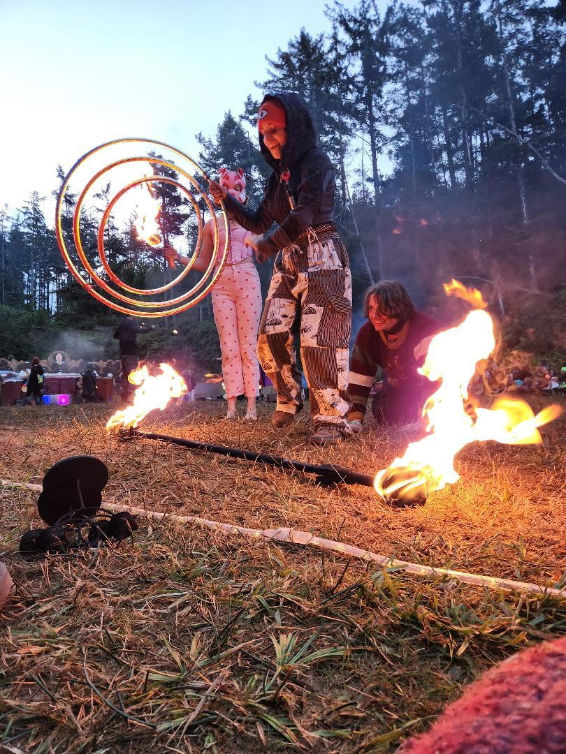 three fire spinners in the circle, one's a dog playing human, one's a human playing dog, one's a human playing with an orbital hoop